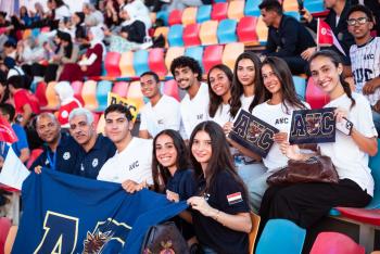AUC students cheer from the stands holding an AUC banner. 