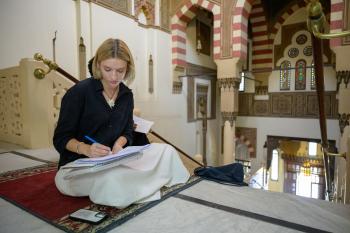 Nina Ellis sits cross legged writing in a notebook at AUC's Tahrir Square