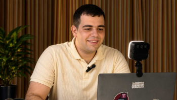 Student in beige shirt smiles in front of laptop