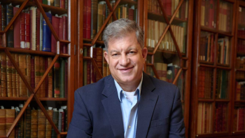 Man in blue suit stands in front of book shelves.