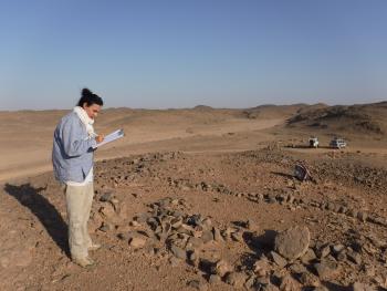 Meredith Brand standing in desert ruins holding a clipboard