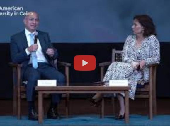 A woman and a man sitting down, the man is talking into a microphone