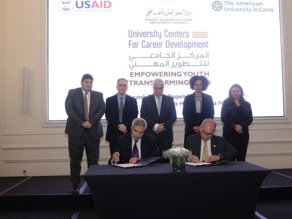 Group of people standing and two men signing contract