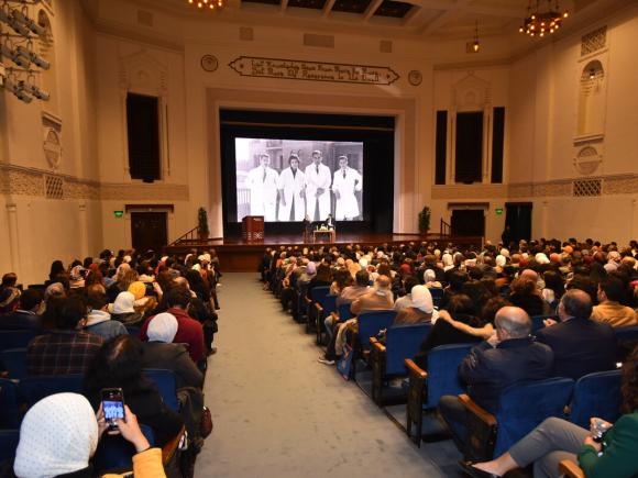 People sitting in a hall listening to people on stage 