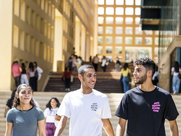 Two boys and a girl walking on campus by building