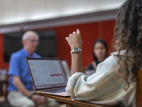 Girl with curly hair sitting in class with a laptop opened and pointing with her hand 