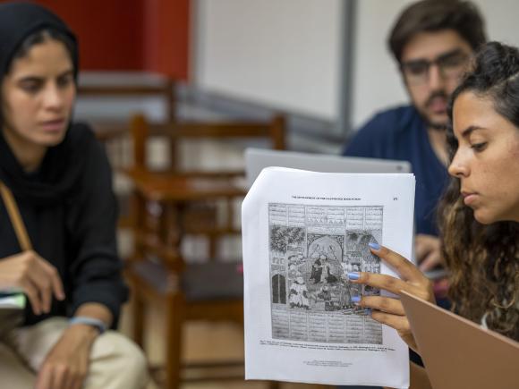 A girl holding a paper explaing to other students in a classroom