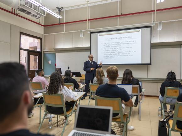 Back view of students in class with a professor explaining from a projector screen