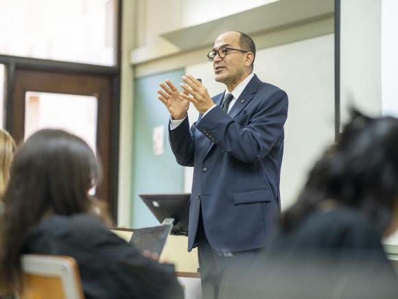 Man wearing a suit and tie in a classroom explaining to students