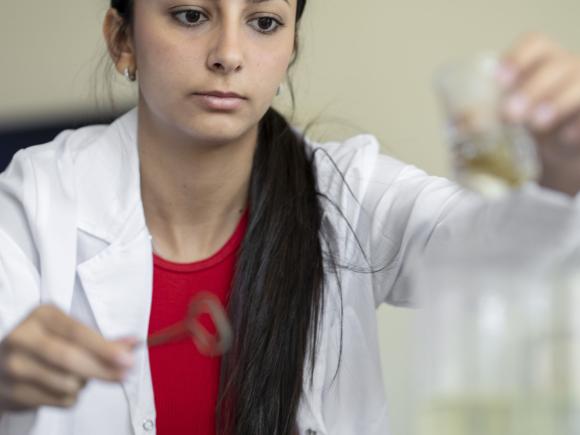 A girl in a lab wearing a white lab coat conducting an experiment using a glass flask