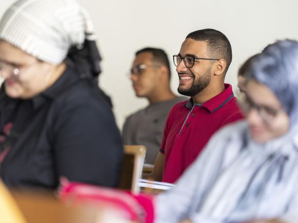 A boy sitting in class with glasses smiling 