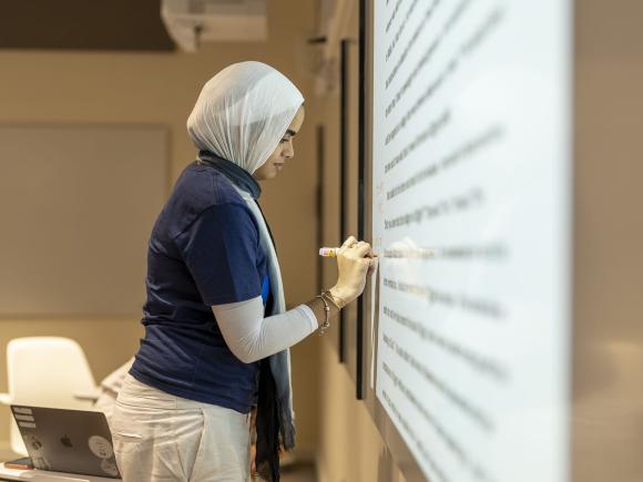 Female student writing on a screen in class