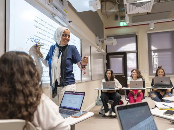 A female student is standing in front of a screen and writing on it