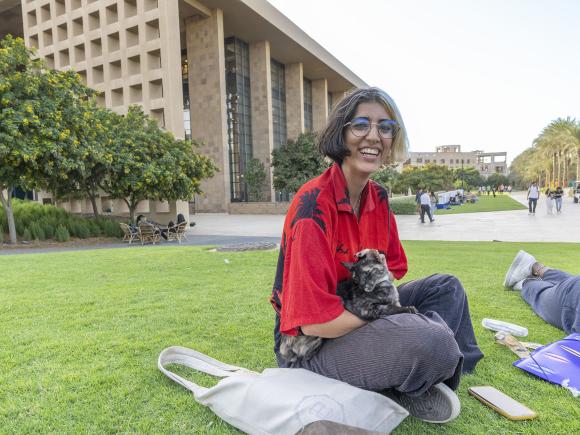 Female student smiling and sitting in the garden stroking a cat sitting on her lap