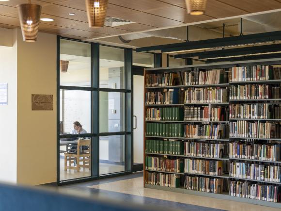 Female student studying in a glass room in the library next to book shelves