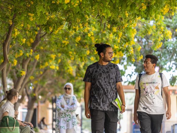 Two male students walking and talking by bus gate