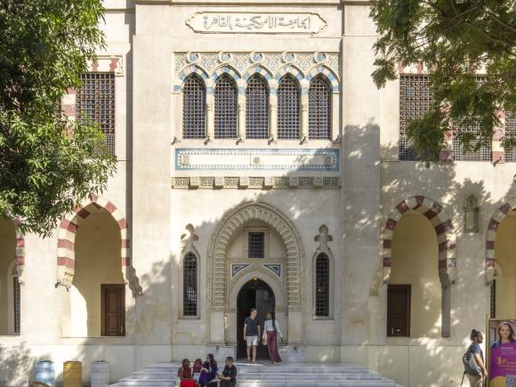 Female and male students walking on campus in front large Islamic building with three flags on the top