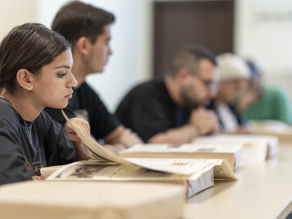 Girl sitting in a classroom flipping page of book infront of her