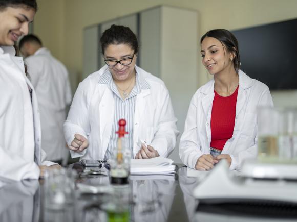 biology program image of group of  female students in white coats working with science equipment 
