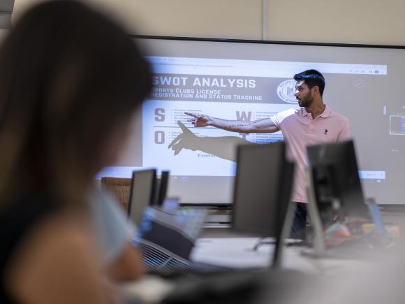 student in class presenting in front of other students on white board