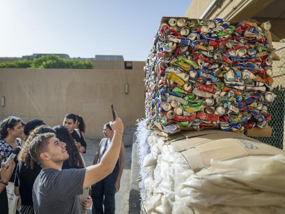 student taking a photo with his phone of the large pile of recycling packed soft drinks pile ready for recyling