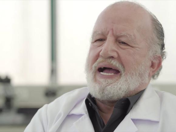 Man wearing a white coat in a lab talking