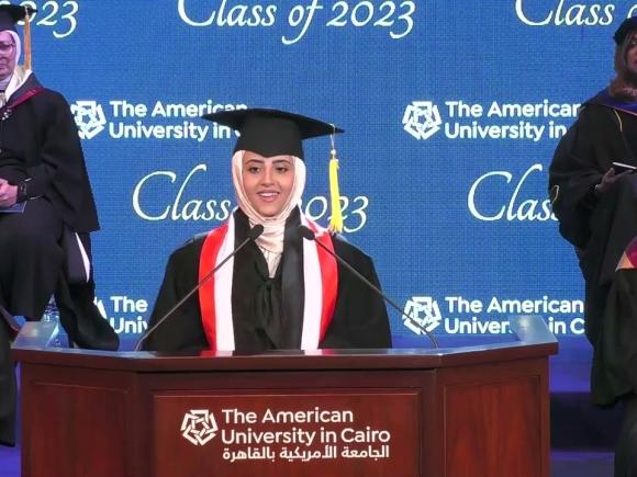 Female speaking at podium wearing her cap and gown