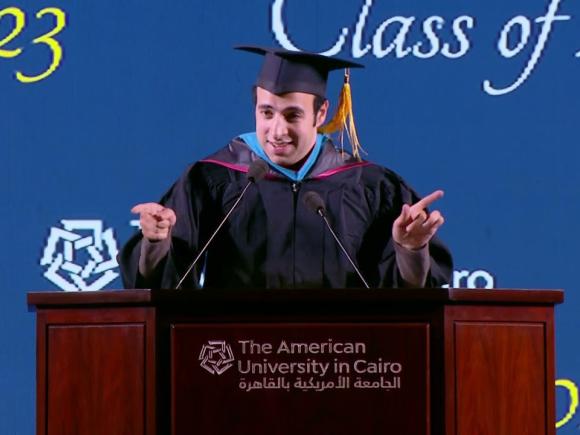 Male wearing his cap and giving a speech at a podium