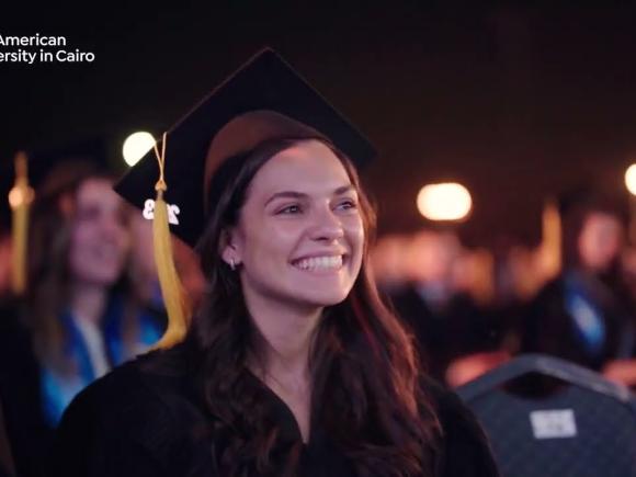 A female is smiling and wearing her cap and gown during graduation