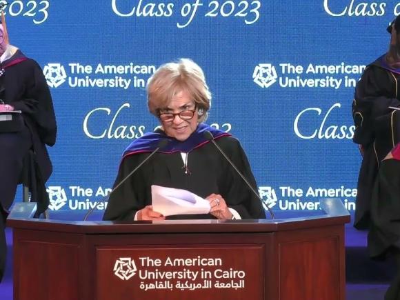 Woman wearing a gown, standing at a podium and giving a speech