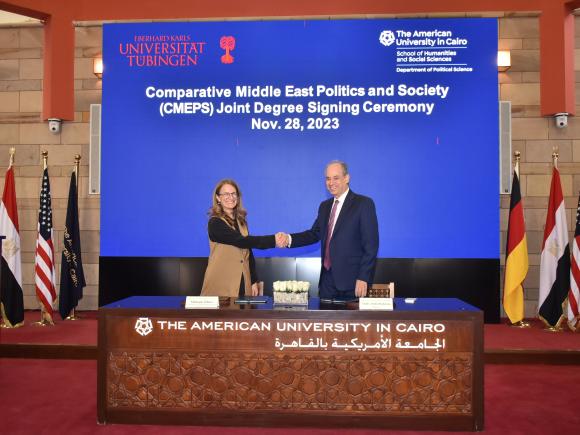 A man and a woman shake hands in front of a blue background