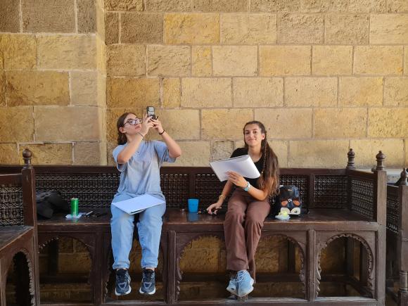 2 students in an old historical location, one taking pictures and the other holding a sketching paper