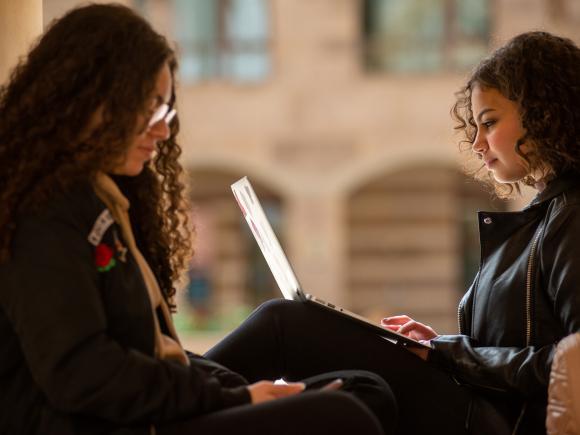 Two girls sitting together with one girl holding a laptop