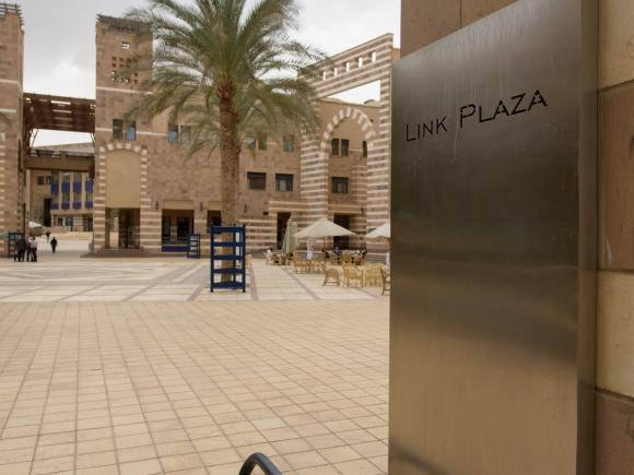Campus view of Link Plaza with stone buildings, palm trees, and outdoor seating areas.