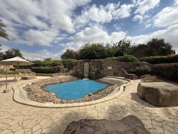 Outdoor campus garden with a small waterfall flowing into a blue pool surrounded by stone seating and greenery.