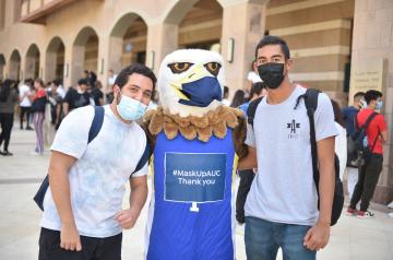 Two AUC students with masked mascot
