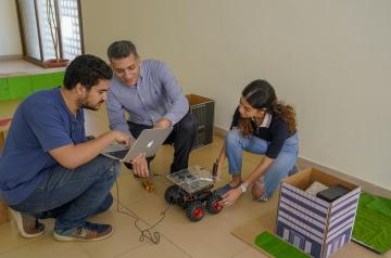 Two men and onw woman sitting on the floor holding a to car