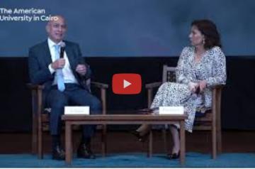 A woman and a man sitting down, the man is talking into a microphone