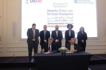 Group of people standing and two men signing contract