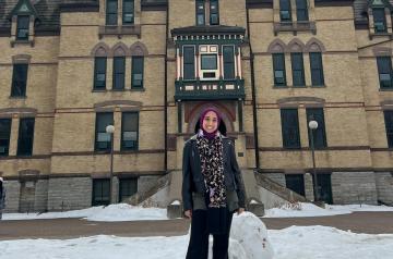 Female student standing in the snow in front of an old building