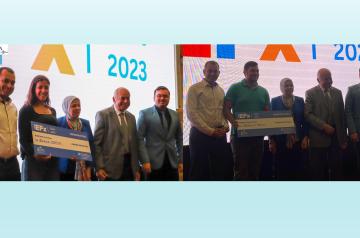 Zahwa Kortam and Abdallah Sabah accept their awards standing on stage in front of a screen.
