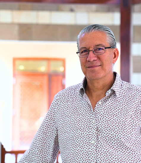 Man standing, wearing a shirt and glasses and smiling