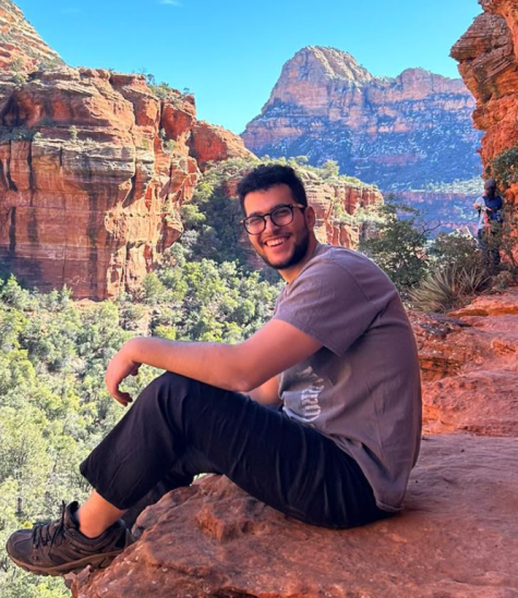 A male wearing glasses is sitting on a mountain