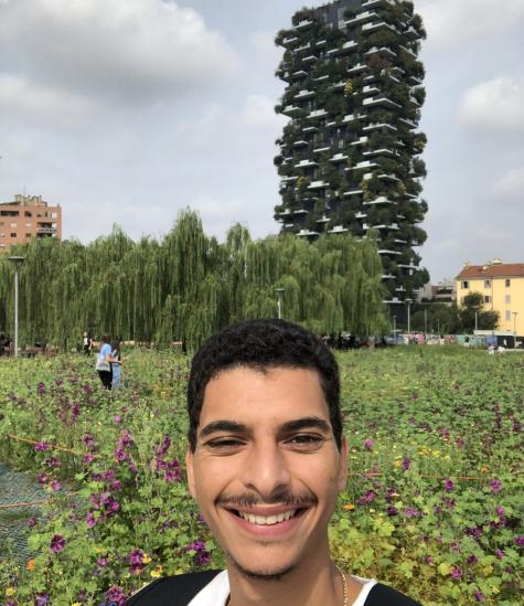 A male is standing in a green field in front of a tall building filled with greenery