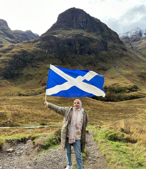 A female is standing in green highlands holding the flag of Scotland