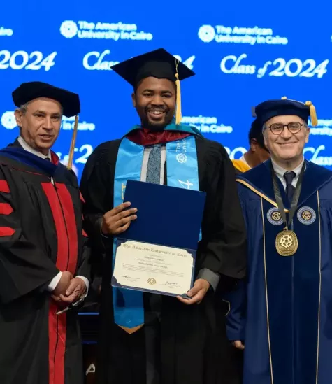 a graduating student standing on stage holding his certificate with two men standing beside him