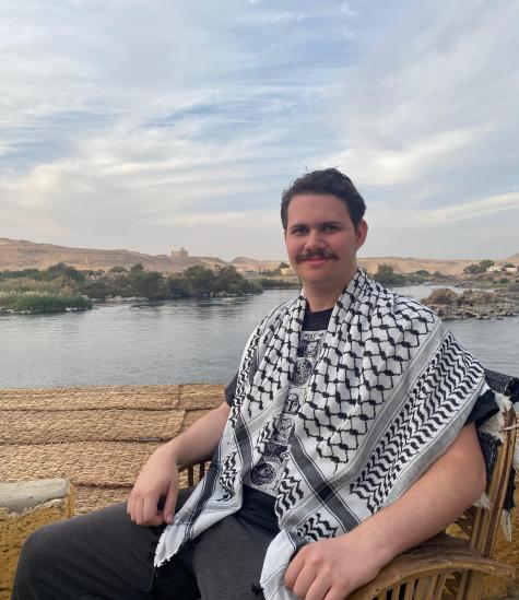 Finn smiles at the camera in front of a lake, wearing a black and white keffiyeh.
