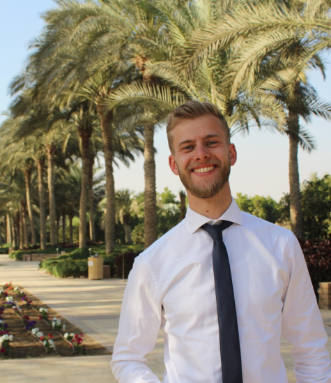 Frederik smiles for a headshot in front of the palm trees in the AUC garden.