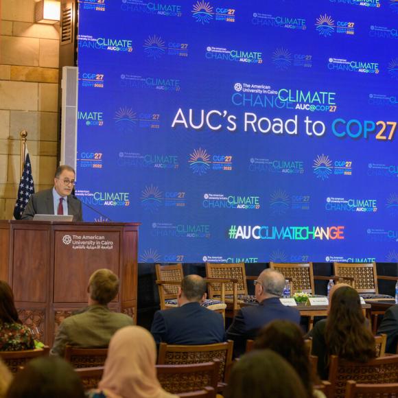 Man is talking into a microphone on a podium, AUC's Road to COP27