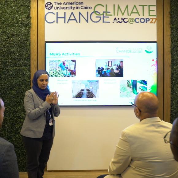 A woman talking to an audience and standing next to a screen